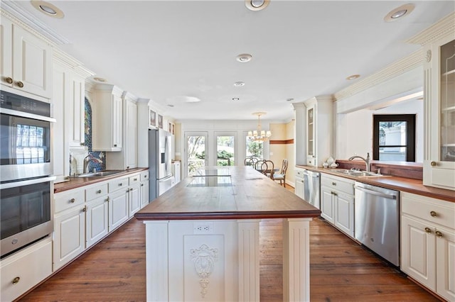 kitchen with stainless steel appliances, a sink, wood counters, a center island, and an inviting chandelier