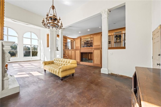 living area featuring decorative columns, a fireplace with raised hearth, and concrete flooring