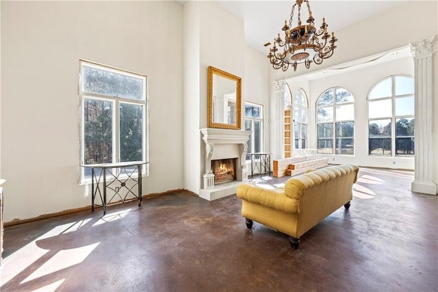 living area with finished concrete floors, a wealth of natural light, a warm lit fireplace, and ornate columns