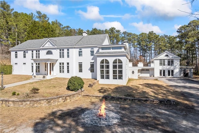 view of front facade featuring driveway, an outdoor fire pit, a chimney, and stucco siding