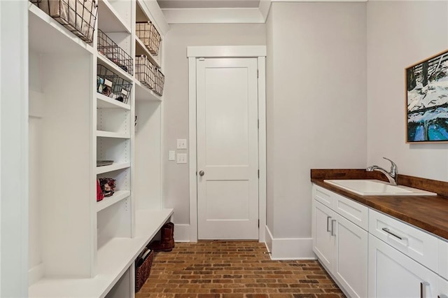 interior space featuring brick floor, a sink, and baseboards