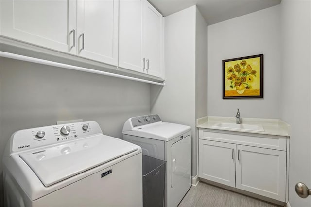 laundry area featuring light wood finished floors, independent washer and dryer, a sink, and cabinet space