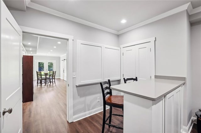 interior space with dark wood-type flooring, white cabinets, crown molding, and a breakfast bar area