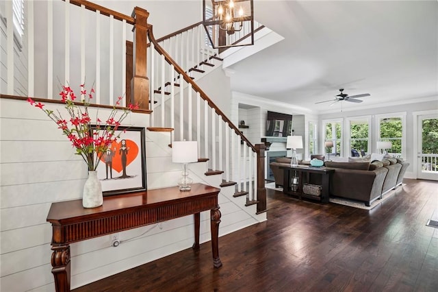 entryway with hardwood / wood-style flooring, ceiling fan with notable chandelier, a fireplace, ornamental molding, and stairway