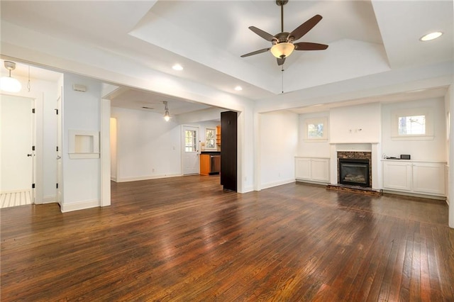 unfurnished living room with a fireplace, a tray ceiling, ceiling fan, and dark wood-type flooring