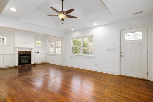 unfurnished living room with ceiling fan, dark wood-type flooring, vaulted ceiling, a tray ceiling, and a fireplace