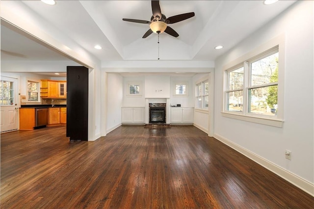 unfurnished living room with a raised ceiling, ceiling fan, and dark hardwood / wood-style floors