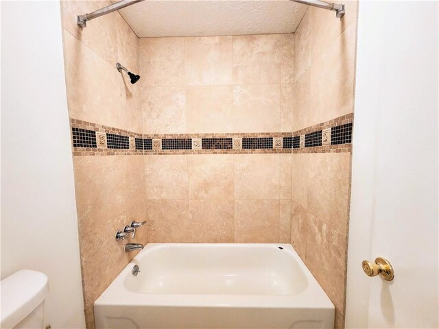 bathroom with tiled shower / bath combo, toilet, and a textured ceiling