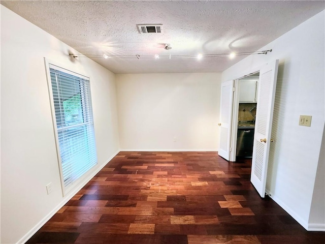 empty room with dark wood-type flooring, a textured ceiling, and rail lighting