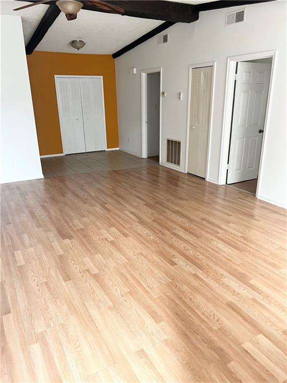 unfurnished bedroom with light wood-type flooring, ceiling fan, two closets, and lofted ceiling with beams