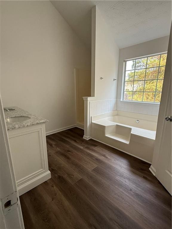 bathroom featuring a bathing tub, a textured ceiling, vaulted ceiling, vanity, and hardwood / wood-style flooring