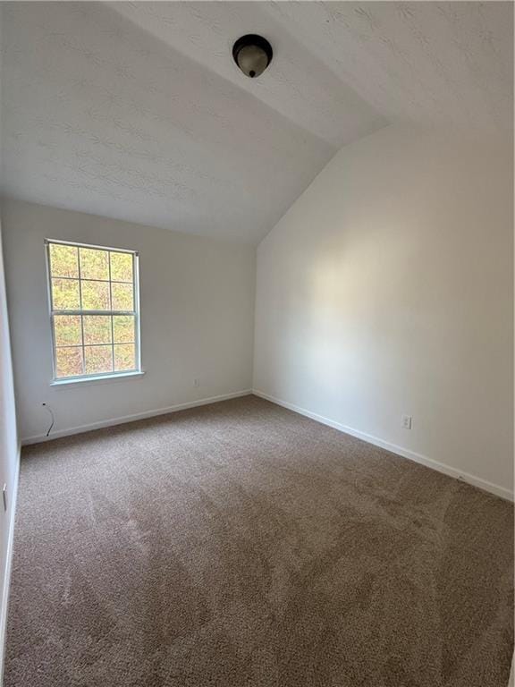 empty room with carpet flooring, a textured ceiling, and vaulted ceiling