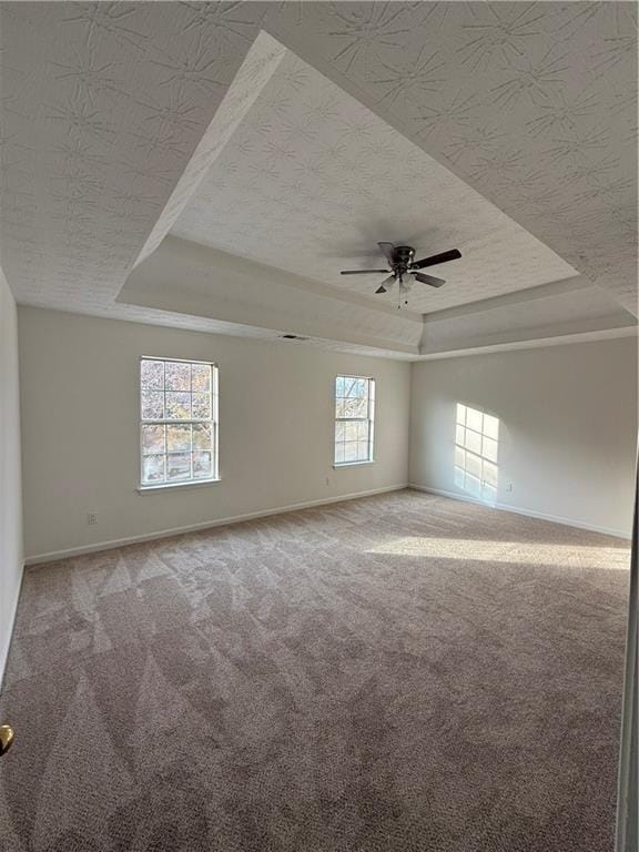 empty room featuring a raised ceiling, ceiling fan, and carpet flooring