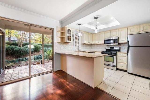 kitchen with appliances with stainless steel finishes, hanging light fixtures, light stone counters, a tray ceiling, and kitchen peninsula