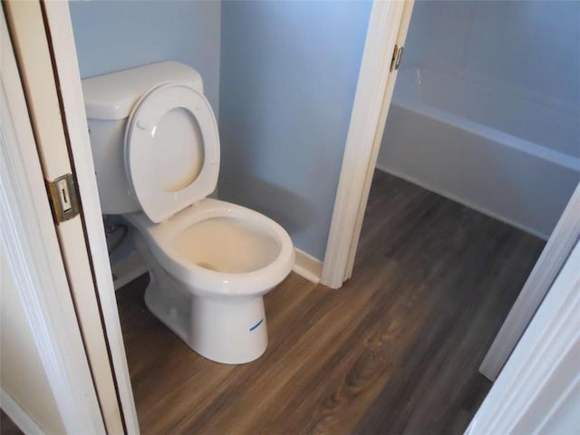 bathroom with wood-type flooring, a tub to relax in, and toilet