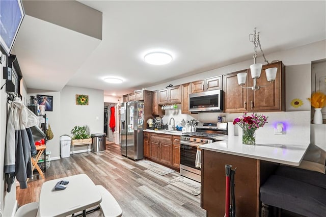 kitchen featuring a peninsula, light countertops, a sink, light wood-style flooring, and appliances with stainless steel finishes