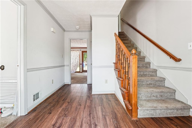 staircase featuring visible vents, a textured ceiling, crown molding, and wood finished floors
