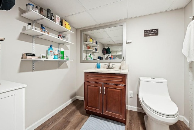 bathroom with vanity, toilet, a paneled ceiling, baseboards, and wood finished floors