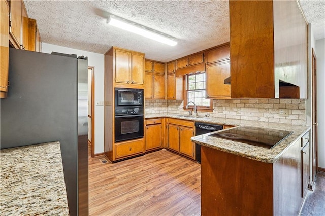 kitchen with backsplash, a sink, black appliances, a peninsula, and light wood-style flooring
