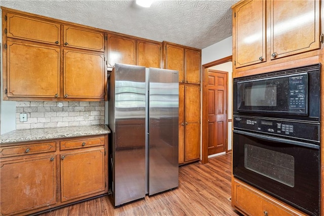 kitchen featuring brown cabinets, a textured ceiling, light wood-type flooring, backsplash, and black appliances