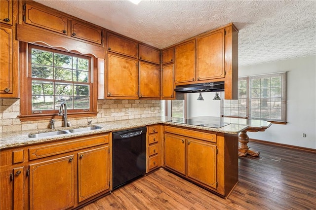 kitchen with brown cabinetry, a textured ceiling, under cabinet range hood, a sink, and black appliances