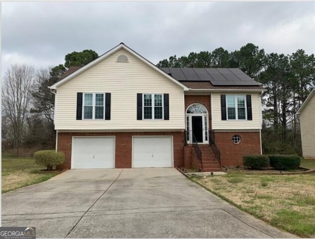 split foyer home featuring a front lawn, solar panels, and a garage