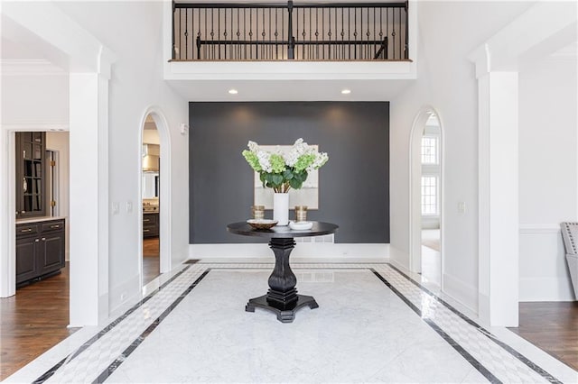 entrance foyer with arched walkways, wood finished floors, a towering ceiling, and baseboards