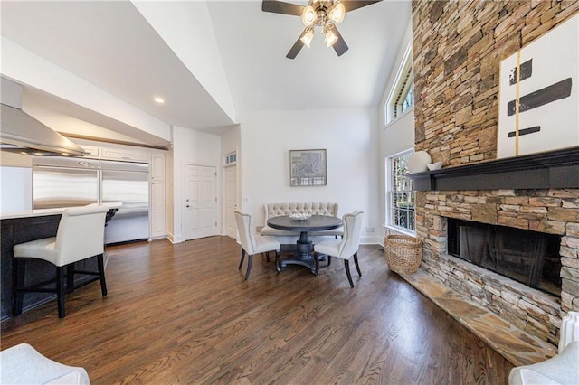 dining room with a ceiling fan, baseboards, a fireplace, high vaulted ceiling, and dark wood-style flooring