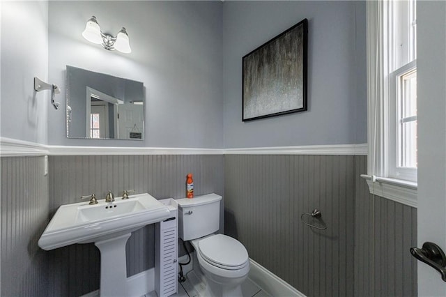 bathroom with toilet, a wainscoted wall, and a sink