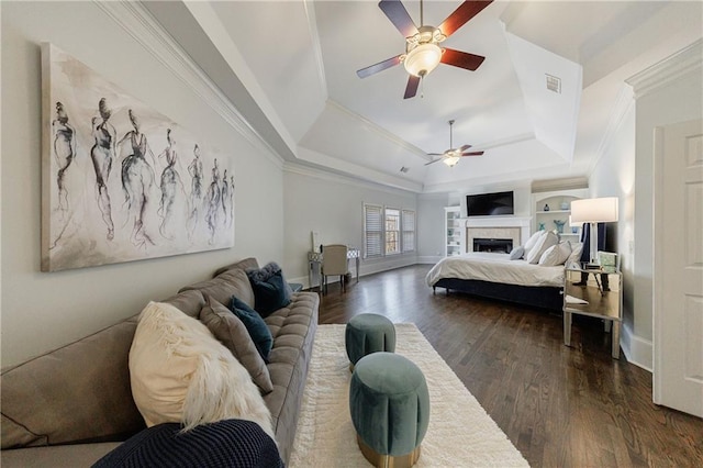 bedroom featuring a tray ceiling, baseboards, dark wood-style flooring, ornamental molding, and a fireplace