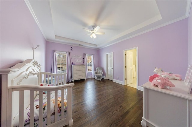 bedroom featuring a tray ceiling, crown molding, baseboards, a crib, and wood finished floors