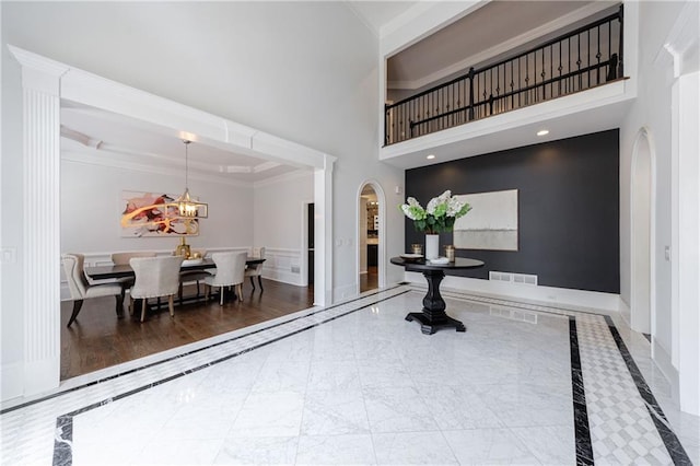 foyer featuring crown molding, visible vents, a chandelier, arched walkways, and a high ceiling