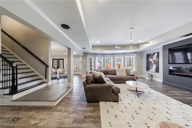 living room featuring a raised ceiling, stairway, wood finished floors, and baseboards