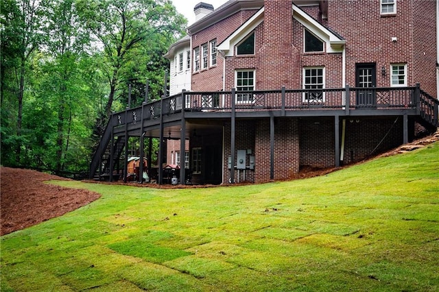 rear view of property with a deck, stairway, brick siding, and a yard