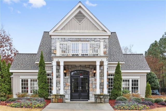 view of front of home with a balcony, stone siding, board and batten siding, and a shingled roof