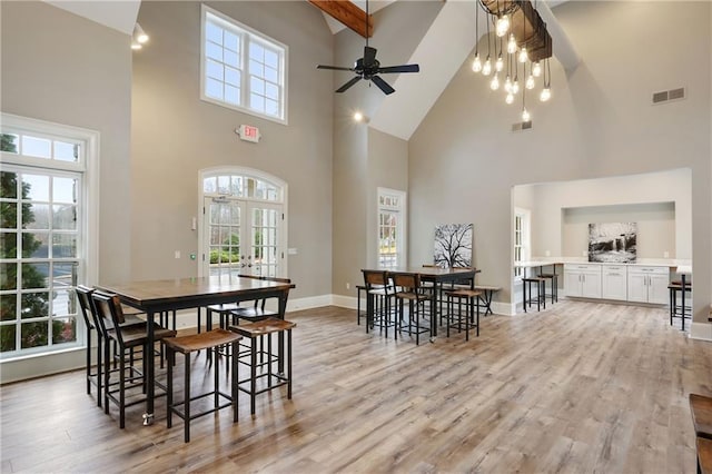 dining space with visible vents, baseboards, light wood finished floors, high vaulted ceiling, and ceiling fan with notable chandelier