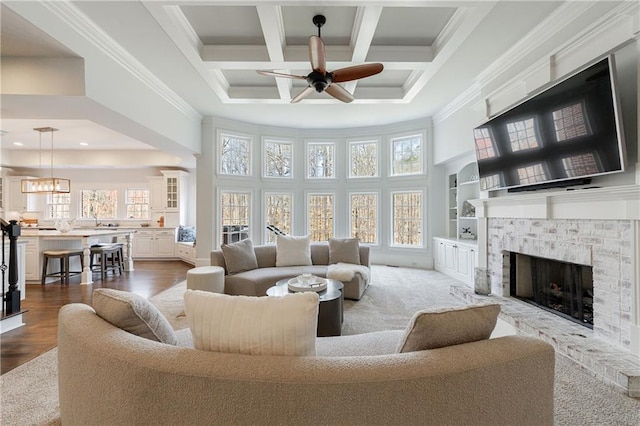living room with coffered ceiling, a ceiling fan, a high ceiling, crown molding, and a fireplace