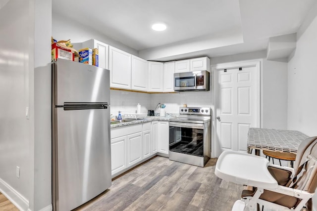 1253 Rivermark Ct, Lawrenceville, GA 30043 - kitchen featuring stainless steel appliances, light wood finished floors, white cabinetry, backsplash, and light stone counters