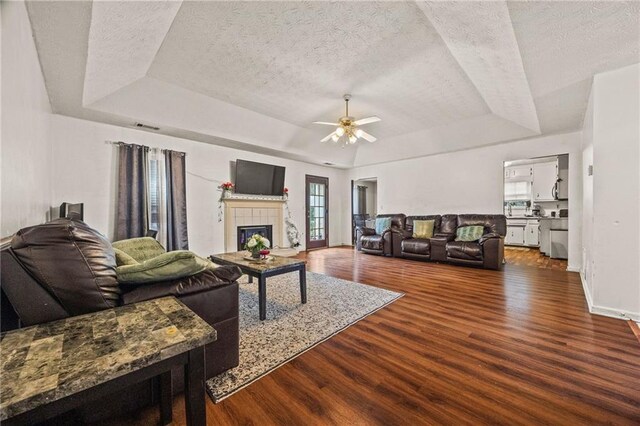 1230 Brook Meadow Ct, Lawrenceville, GA 30045 - living room with a tray ceiling, dark wood-style floors, a ceiling fan, a tile fireplace, and a textured ceiling