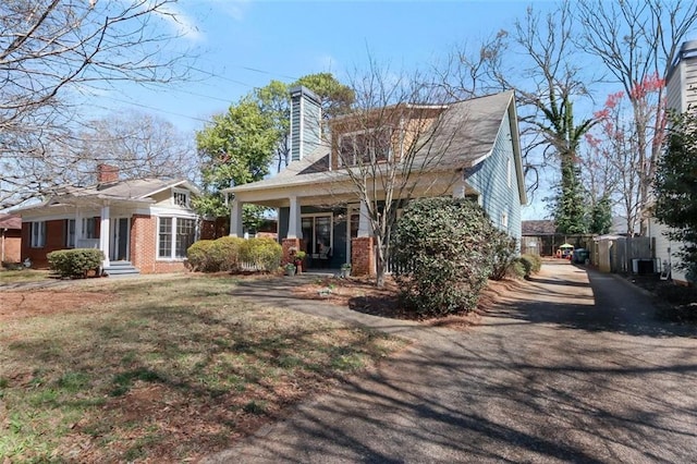 view of front facade with cooling unit, brick siding, a chimney, and driveway