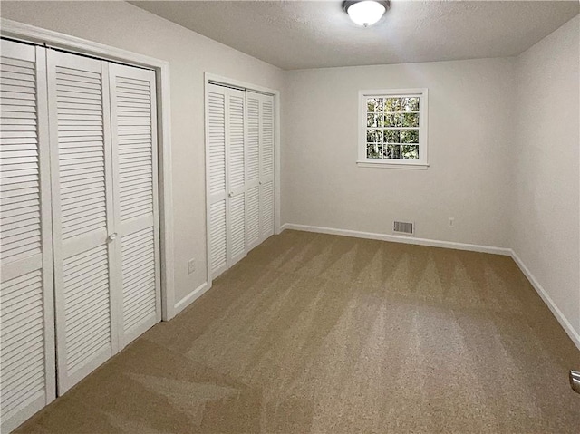 unfurnished bedroom featuring carpet, a textured ceiling, and multiple closets