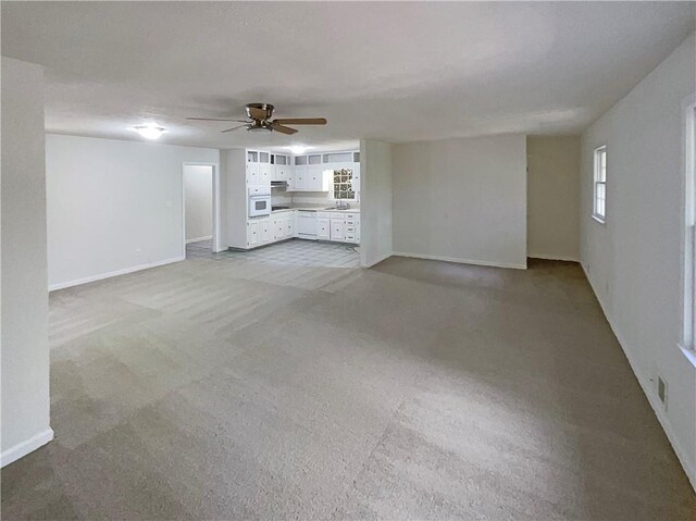 unfurnished living room with light carpet, sink, and ceiling fan