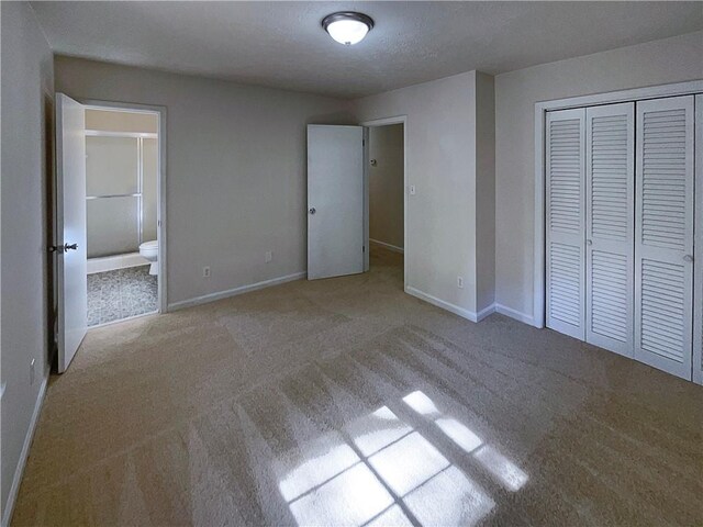 unfurnished bedroom featuring ensuite bath, light carpet, a closet, and a textured ceiling