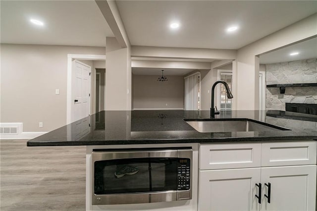 kitchen featuring light wood-type flooring, sink, dark stone countertops, white cabinetry, and stainless steel microwave