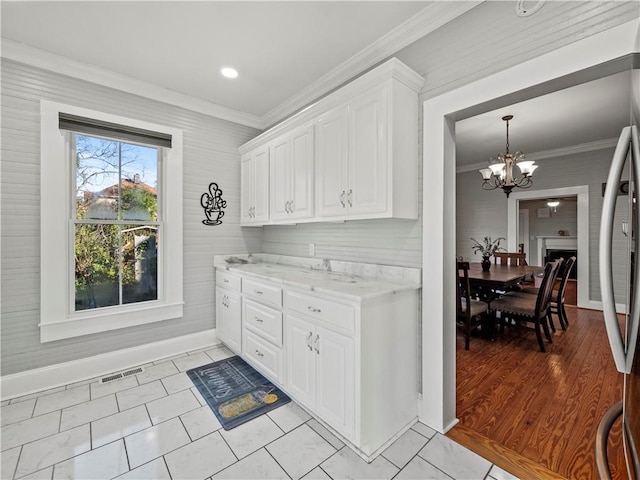 kitchen featuring white cabinets, light stone countertops, ornamental molding, light wood-type flooring, and a notable chandelier