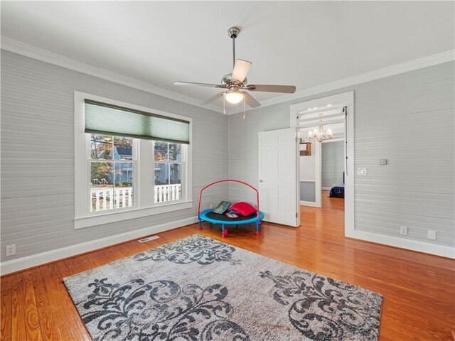 rec room with hardwood / wood-style floors, ceiling fan with notable chandelier, and crown molding