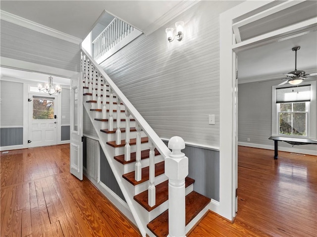 staircase with crown molding, hardwood / wood-style floors, wood walls, and ceiling fan with notable chandelier