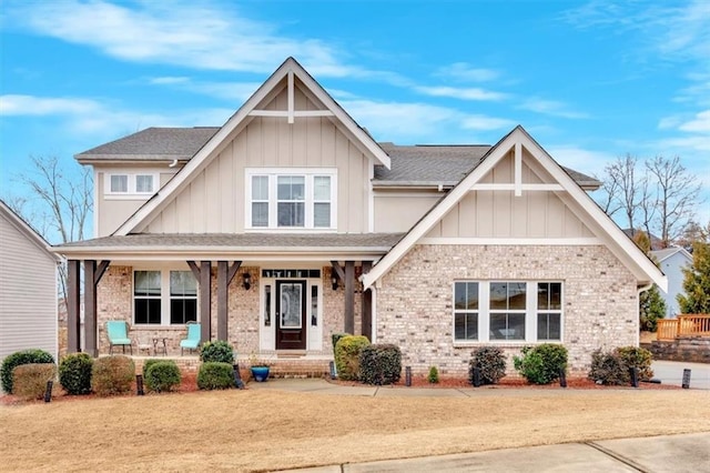 craftsman-style home with board and batten siding, brick siding, covered porch, and a shingled roof