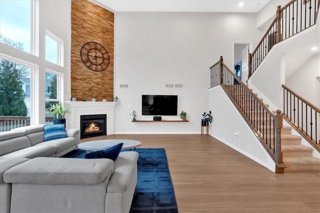 living room with wood finished floors, visible vents, baseboards, a towering ceiling, and a glass covered fireplace