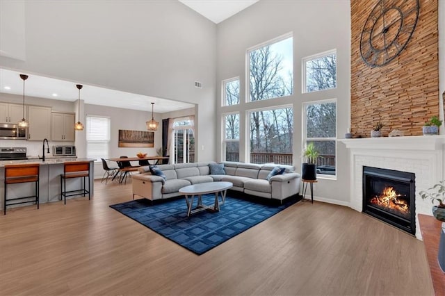 living area featuring visible vents, a brick fireplace, baseboards, and wood finished floors